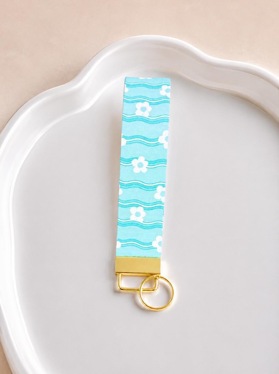 Light blue wristlet keychain with floral pattern and gold clasp on a white plate