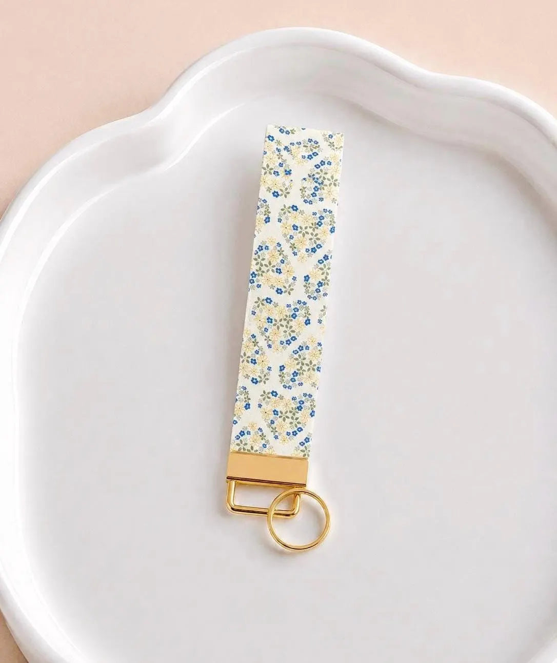 Floral Hearts Wristlet keychain with tiny blue flowers arranged in heart shapes on a cream background with gold hardware on a white ceramic dish
