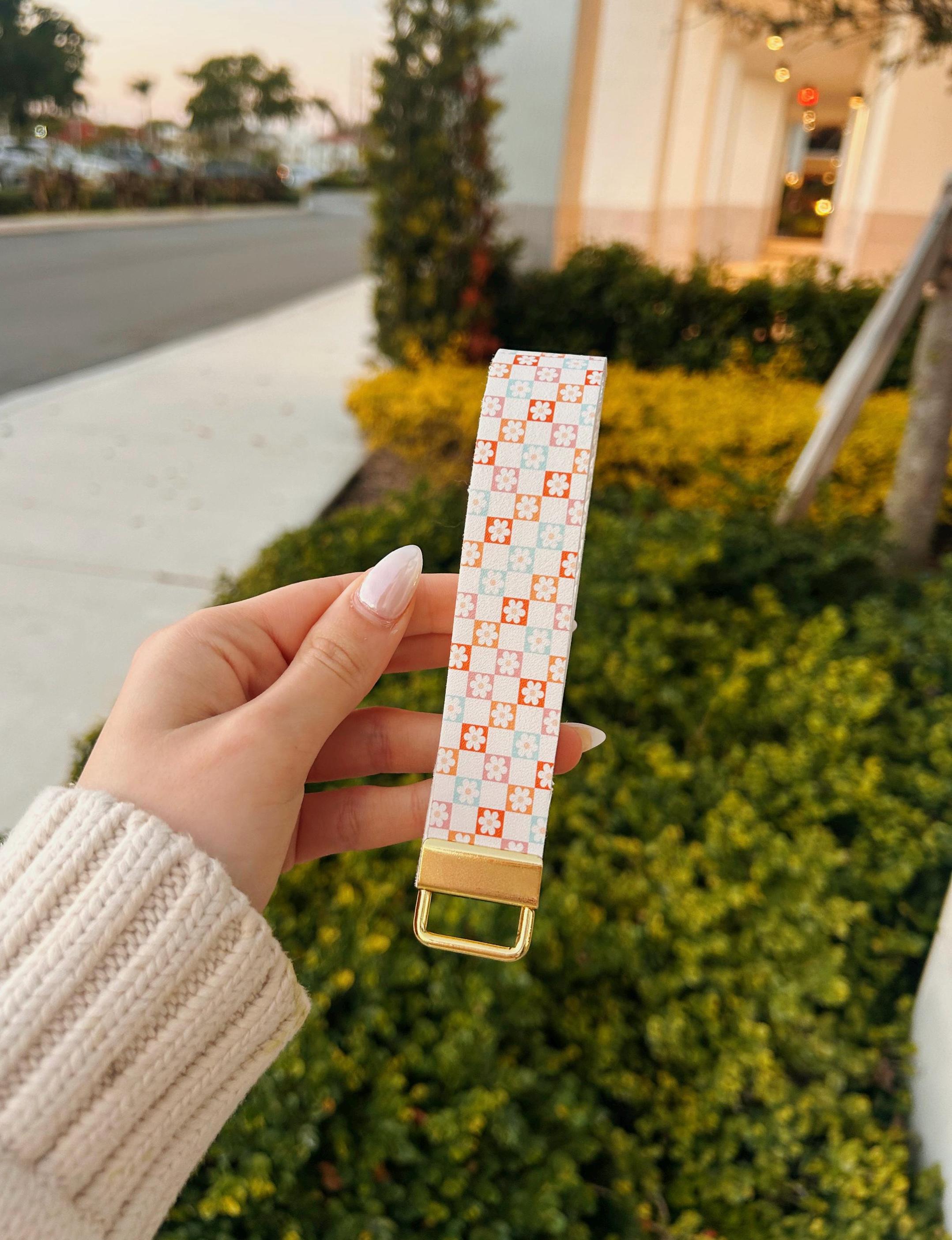 Patterned keychain with gold accent in an outdoor background. White faux leather wristlet keychain with dainty floral tile print in pink coral and mint — Flower Patch Wristlet by Sundazed