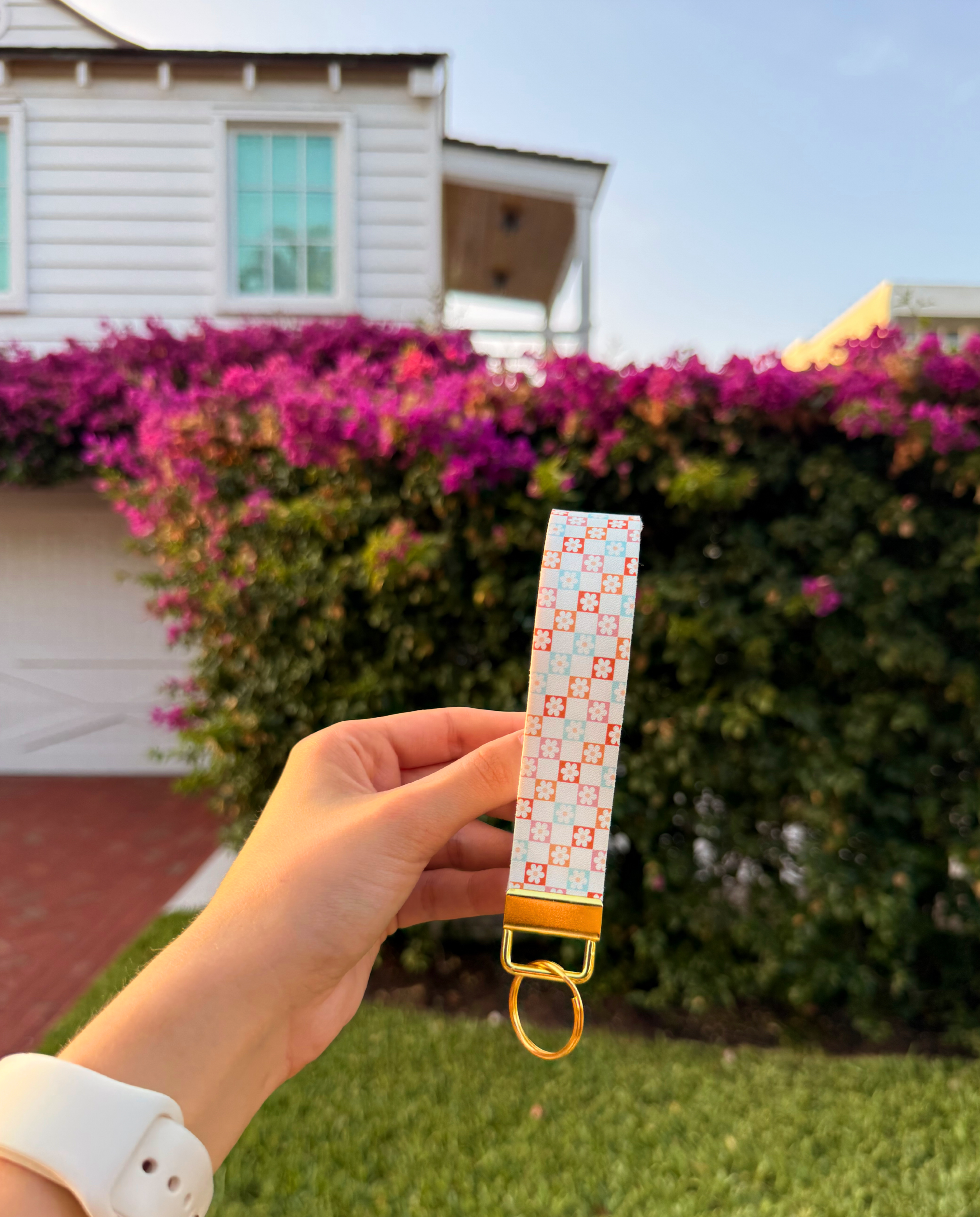Hand holding a patterned keychain with a house and bushes in the background