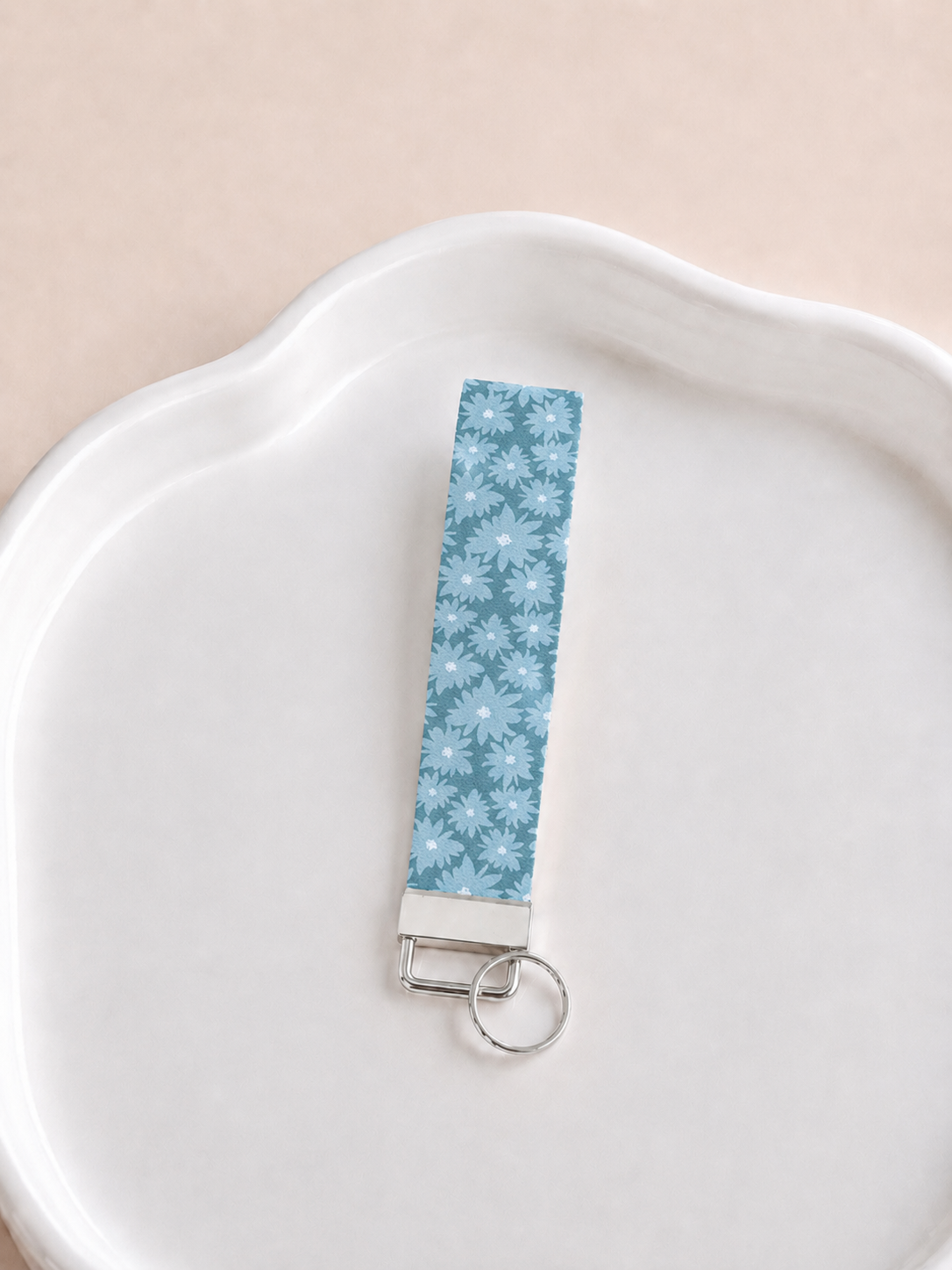 lue Skies wristlet keychain with tone-on-tone daisy floral print in dusty blue, laid on white scalloped tray with silver hardware