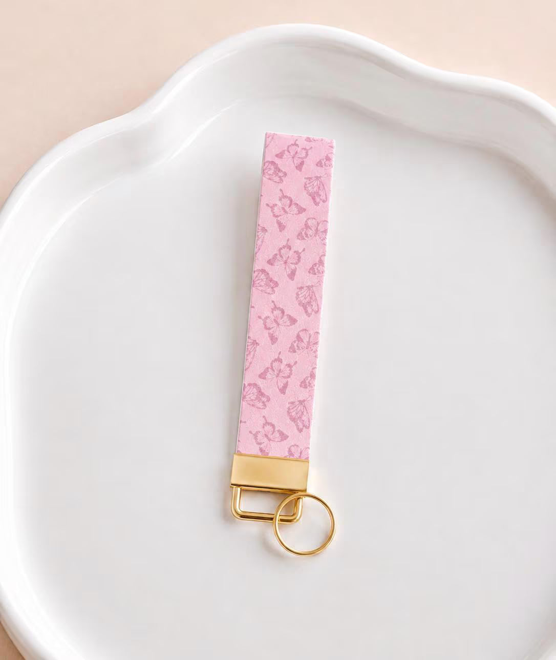 Butterfly Bliss wristlet keychain with soft pink tone-on-tone butterfly print, laid on white scalloped tray with gold hardware