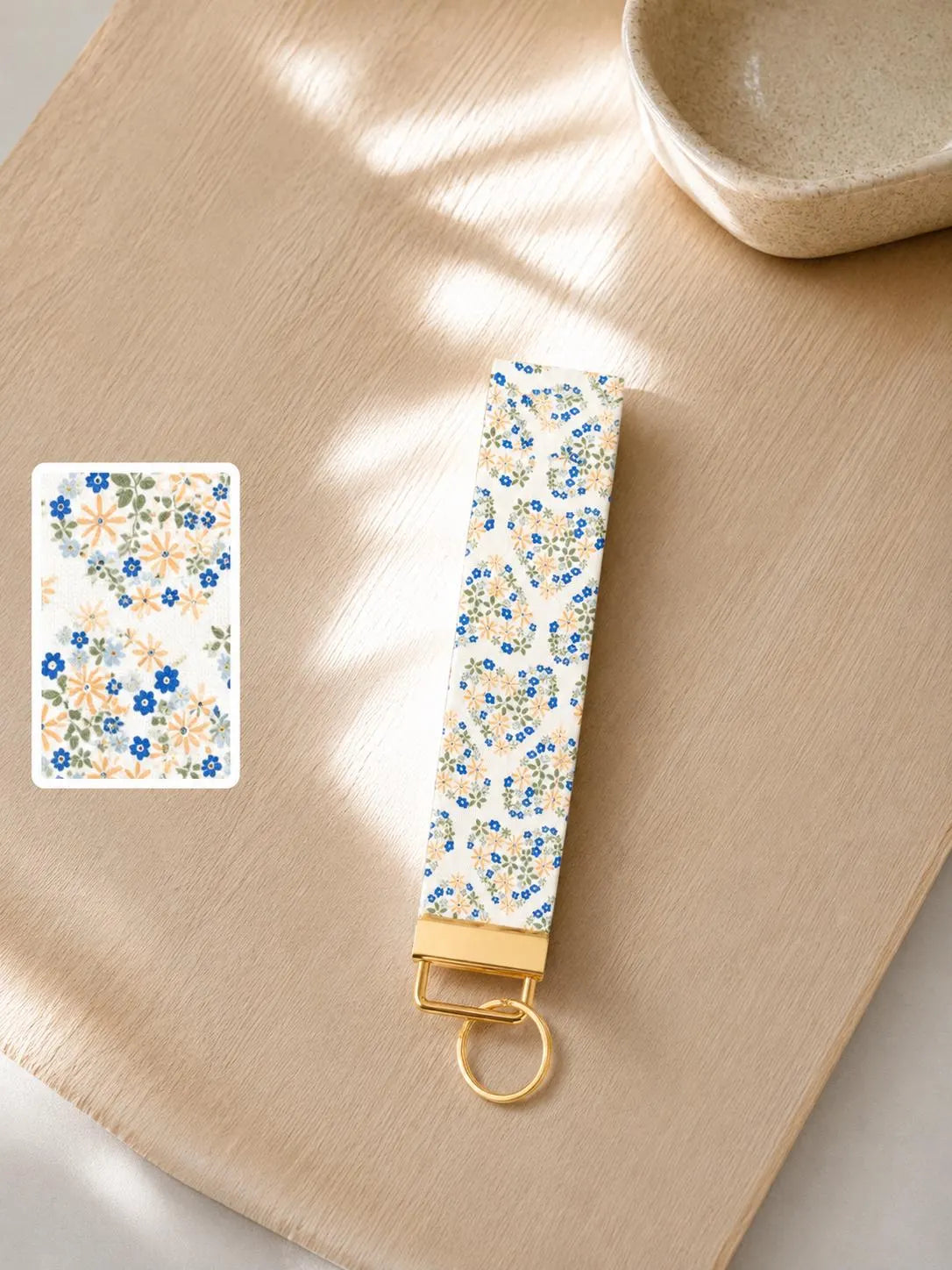 Floral Hearts Wristlet keychain with tiny blue and cream flowers in heart shapes on cream background with gold hardware styled on a wood surface with print detail swatch