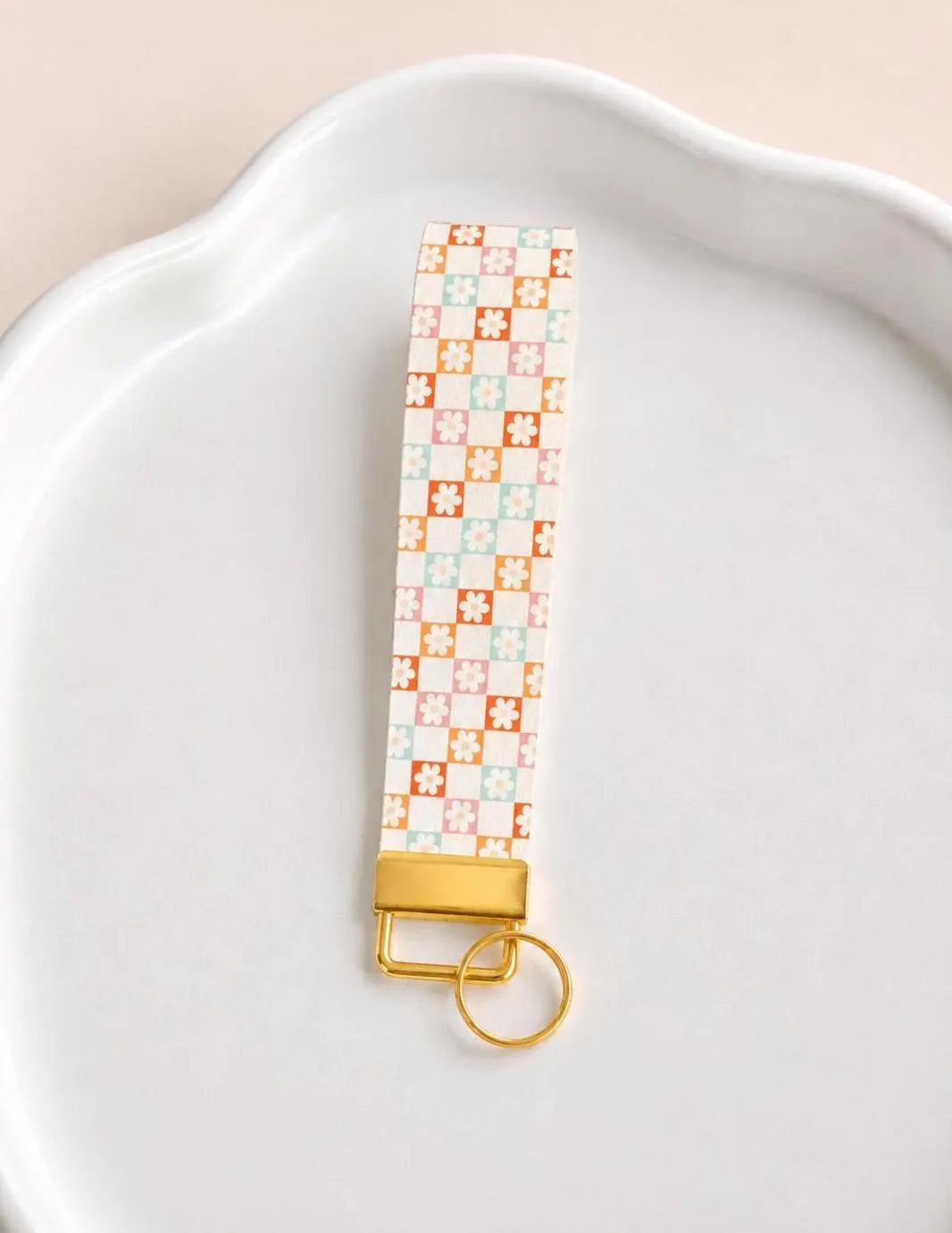 Patterned keychain with gold accent on a white plate. White faux leather wristlet keychain with dainty floral tile print in pink coral and mint — Flower Patch Wristlet by Sundazed