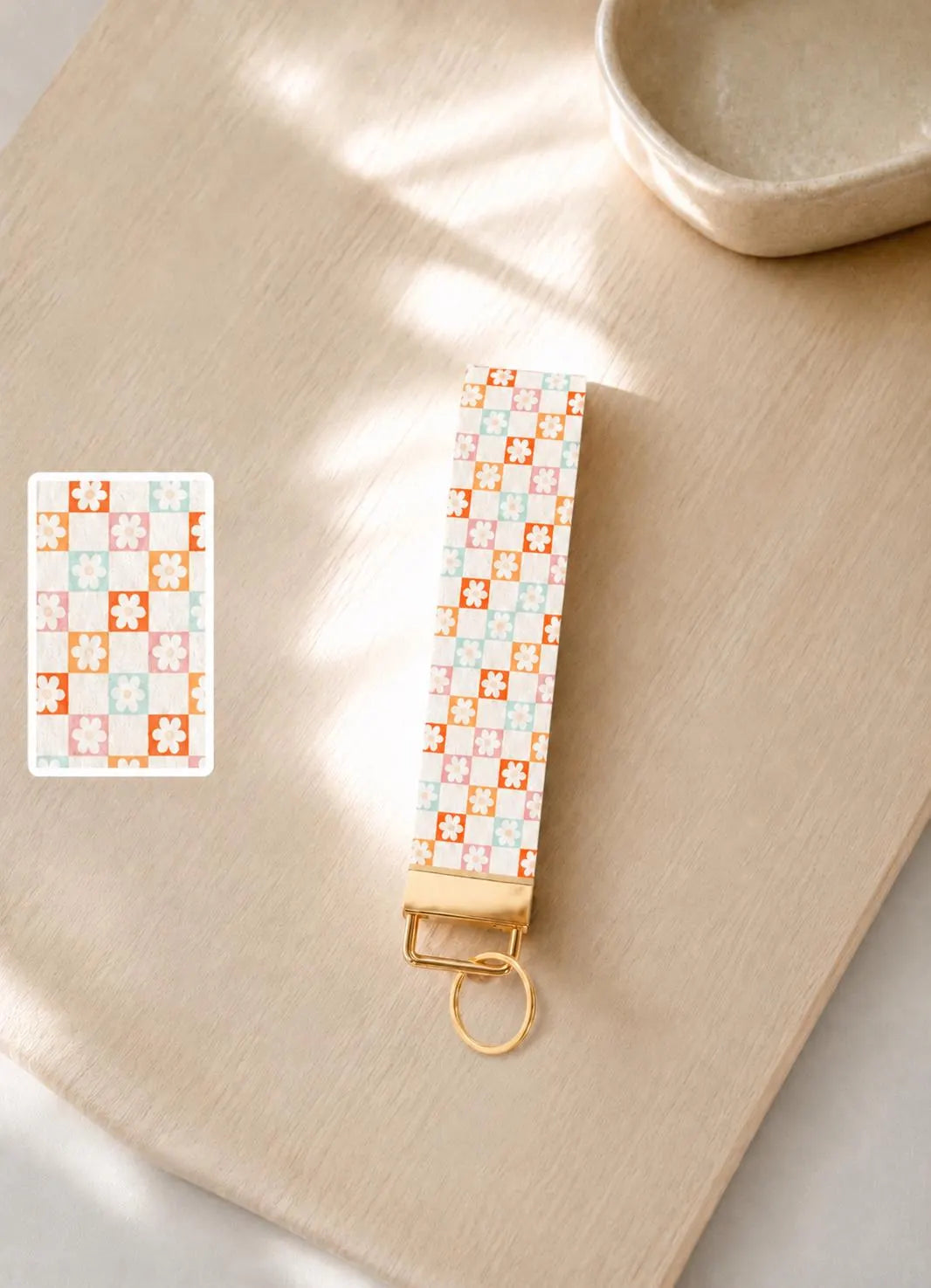 Patterned keychain with gold accent on a wooden platform. White faux leather wristlet keychain with dainty floral tile print in pink coral and mint — Flower Patch Wristlet by Sundazed