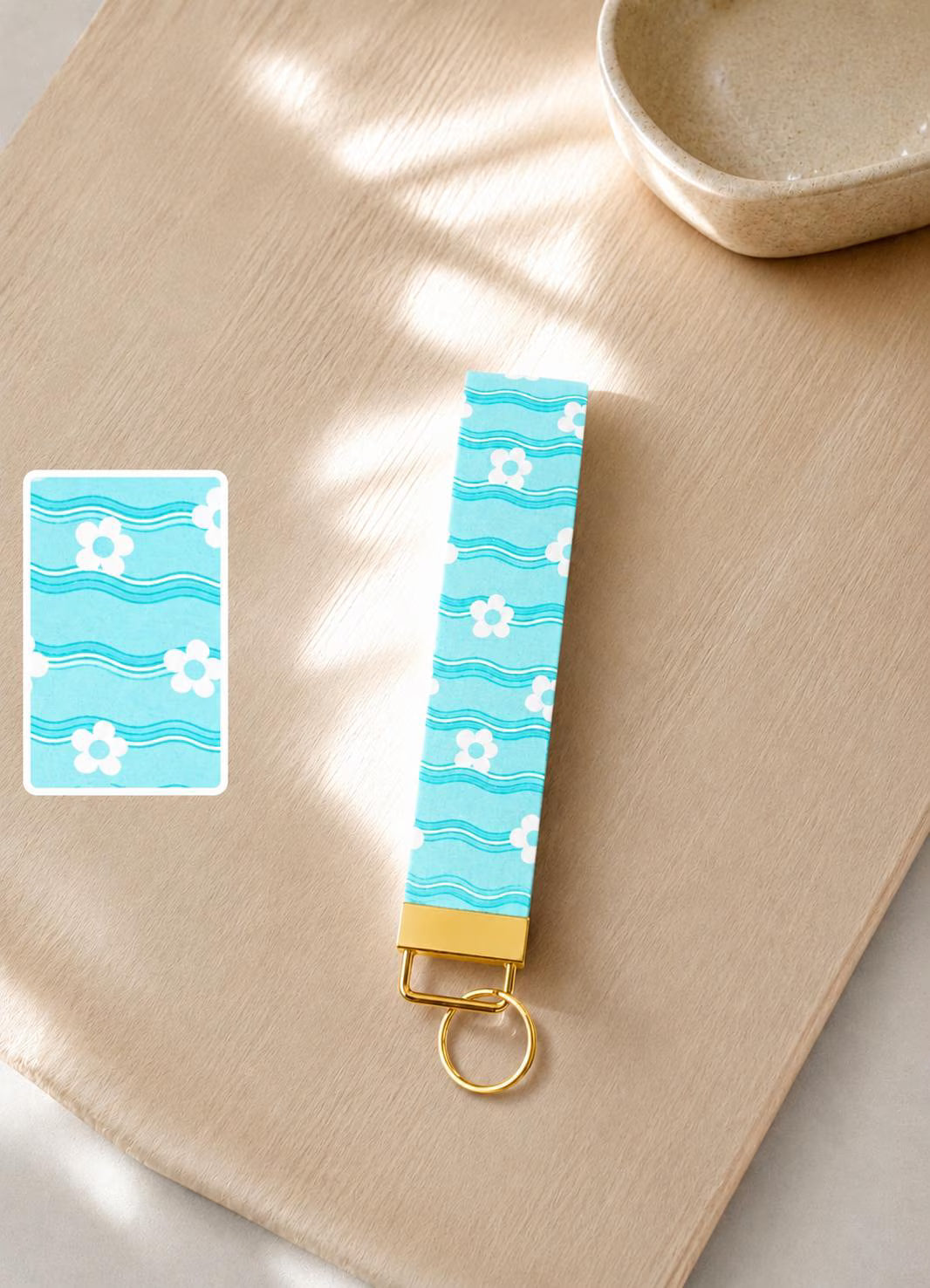 Keychain with blue floral pattern on a wooden surface. Baby blue wave and daisy print wristlet keychain with gold hardware  — Ocean Hues Wristlet by Sundazed
