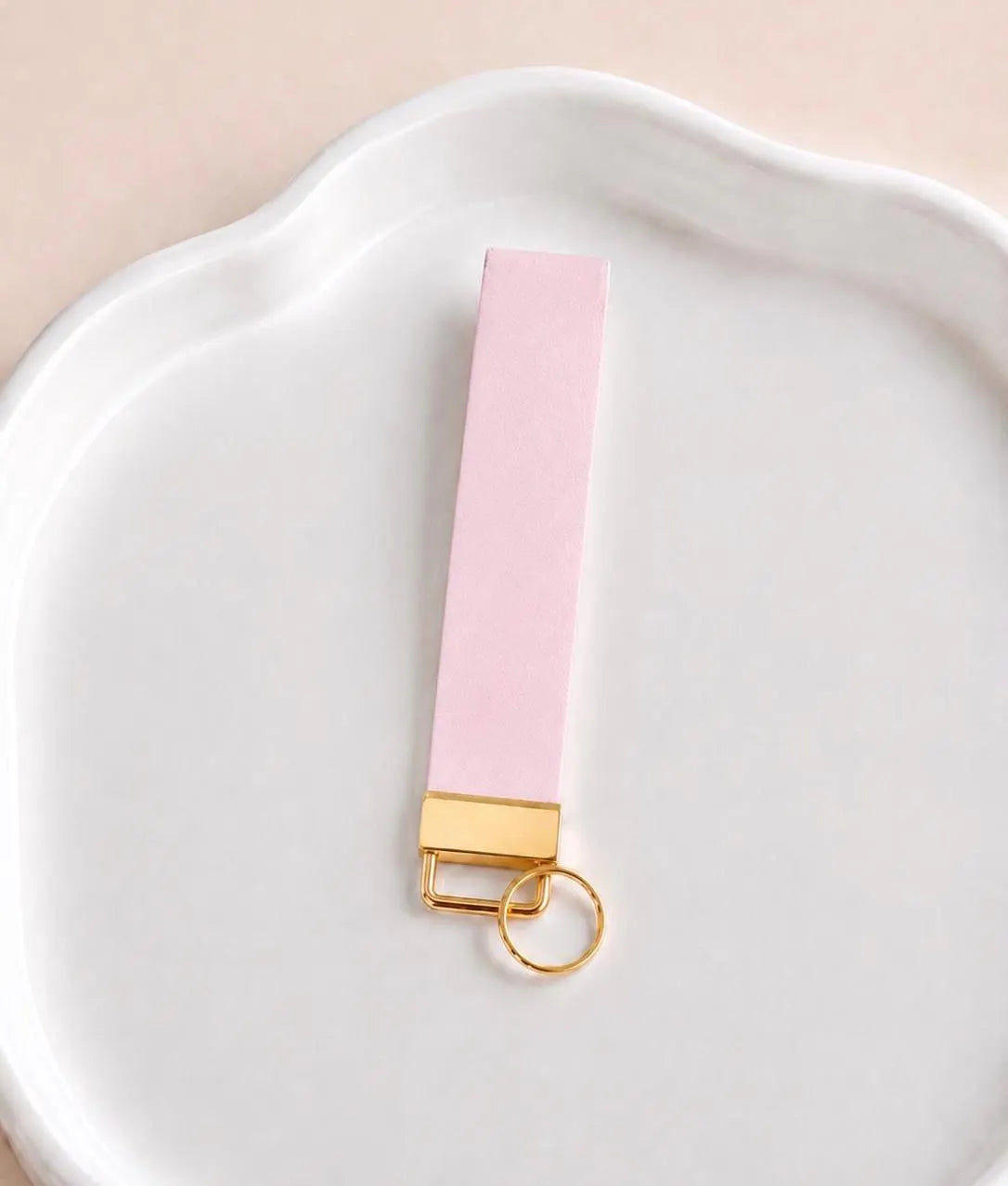 Baby pink faux leather wristlet keychain with gold hardware on white dish — cute pink keychain for women