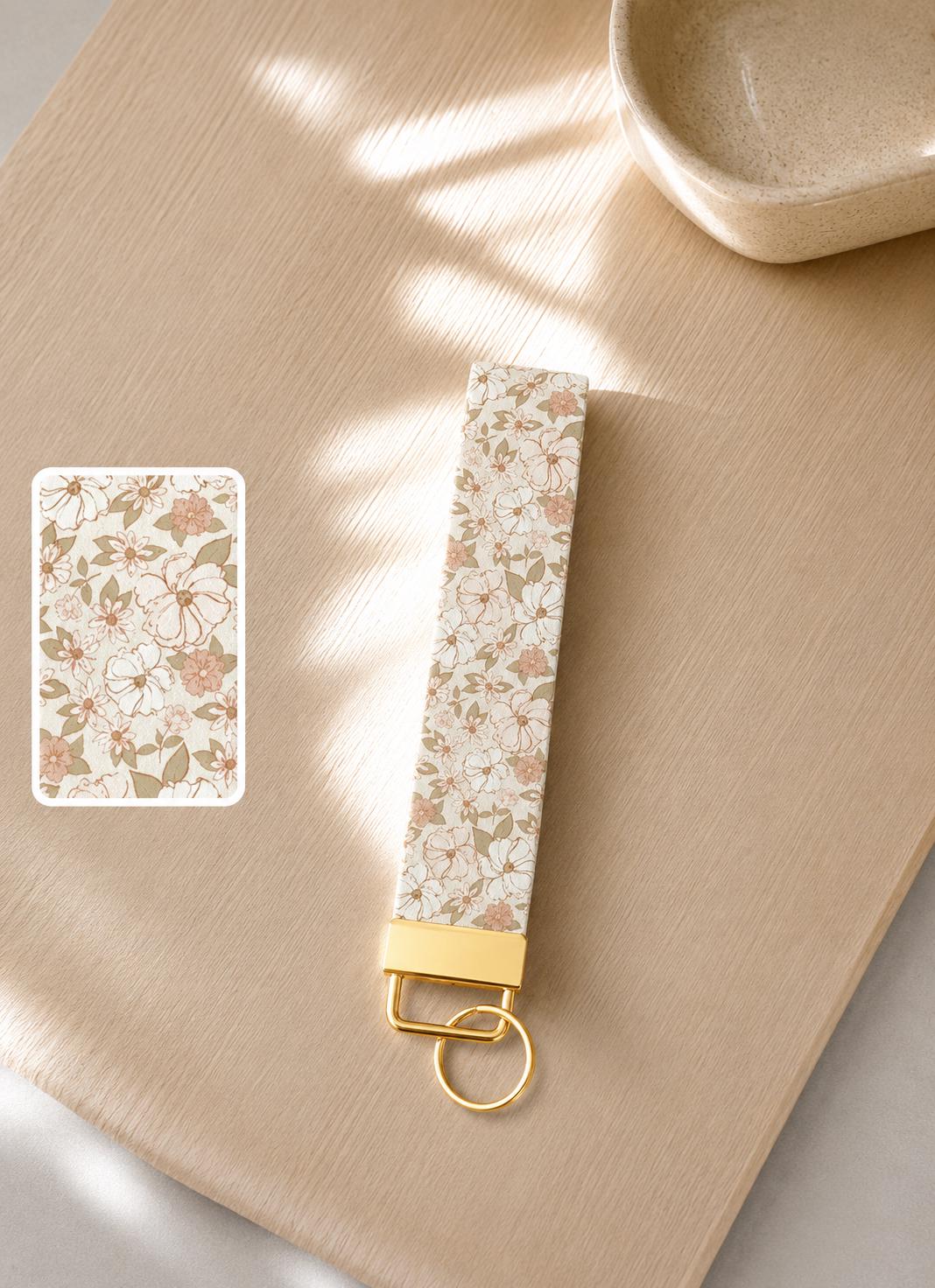Soft Girly Pink Floral patterned keychain with gold accent on a beige wood surface