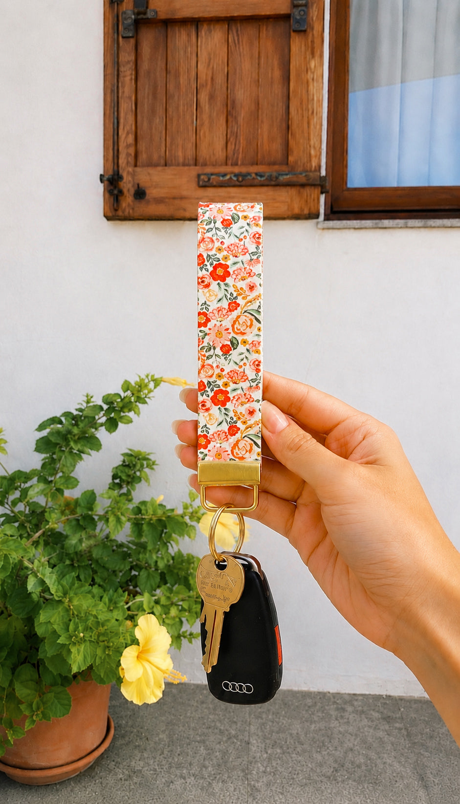 Hand holding Sweet Meadow floral wristlet keychain with keys attached, gold hardware, outdoor setting with yellow flowers