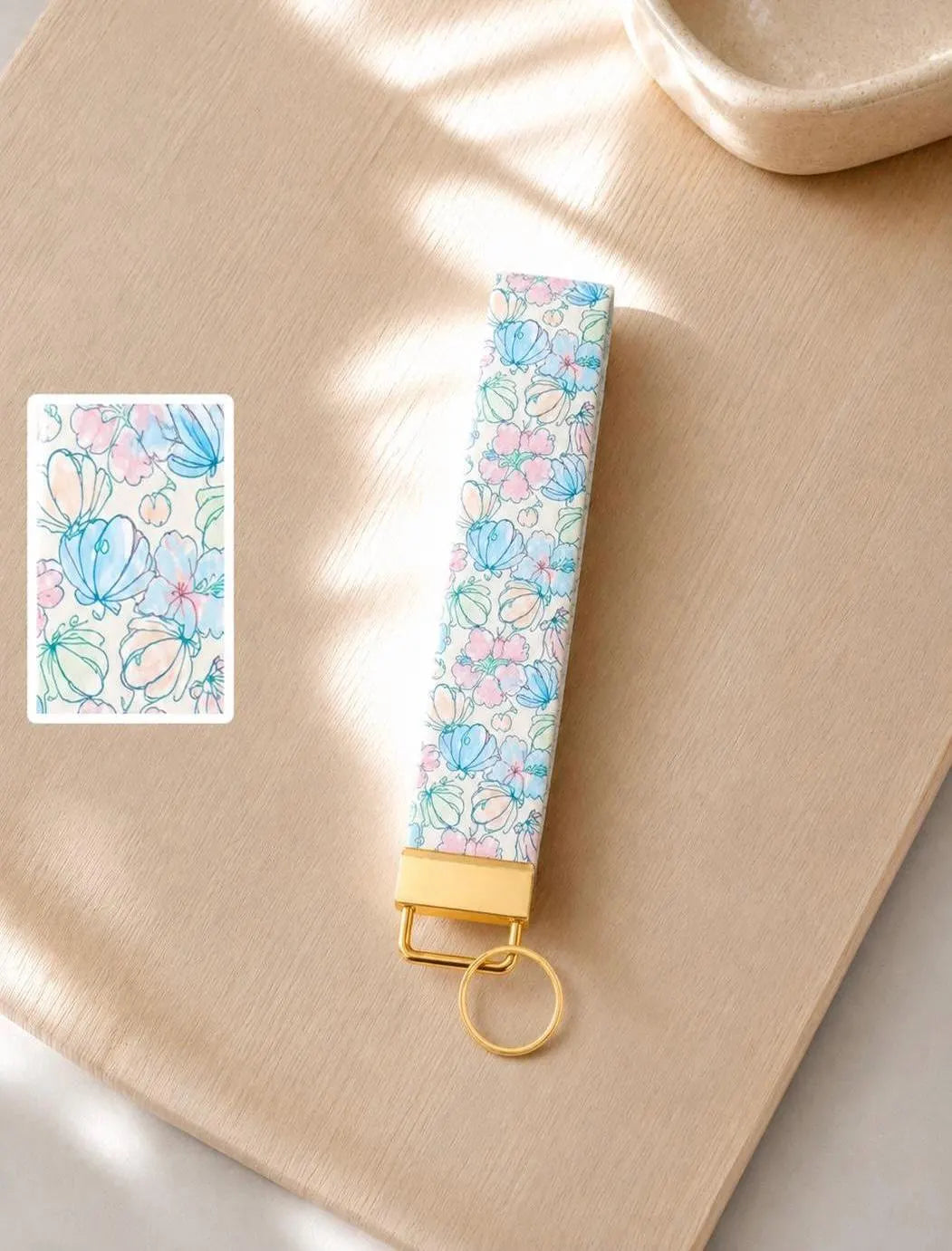 Under the Sea seashell wristlet keychain with watercolor-style aqua and blush floral print on wood surface in natural light with print detail inset and gold hardware