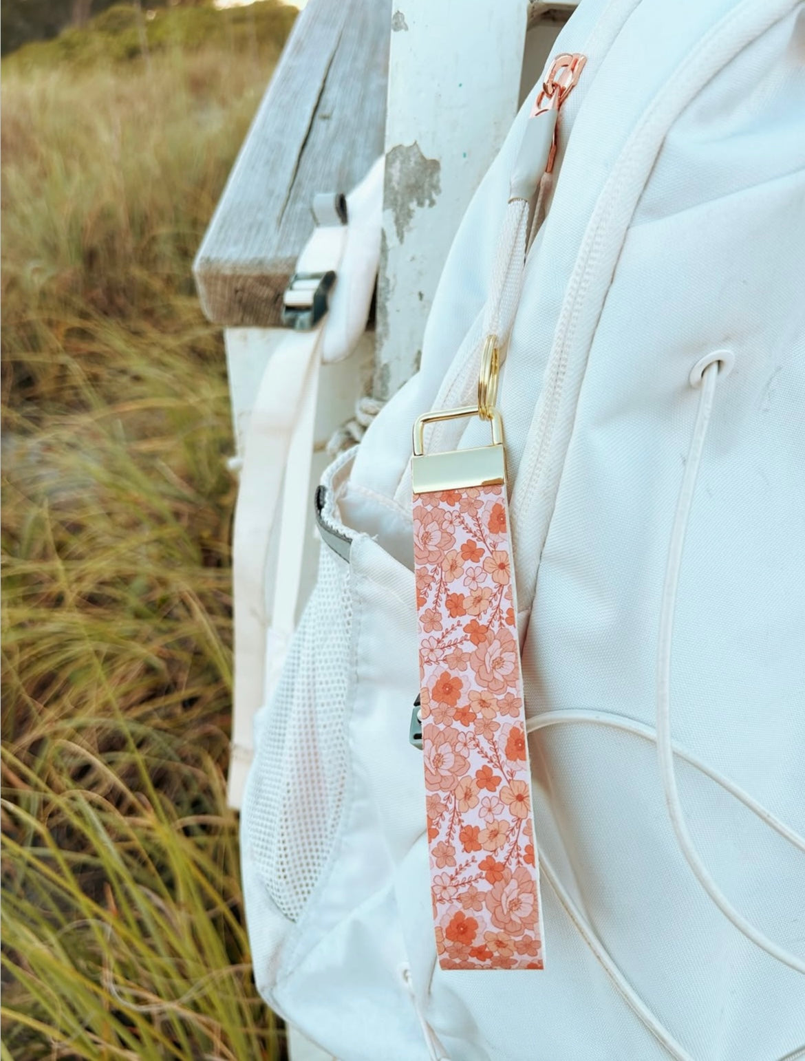 White backpack with a pink wristlet keychain attached to a white backpack in a natural beach setting
