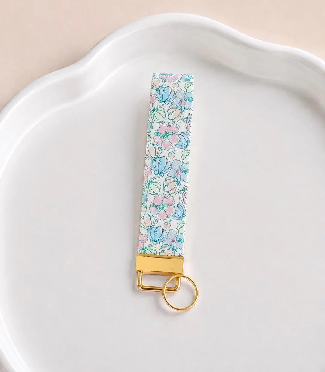 Under the Sea wristlet keychain with delicate line-art floral print in aqua, mint, and blush pink on white, laid on white scalloped tray with gold hardware
