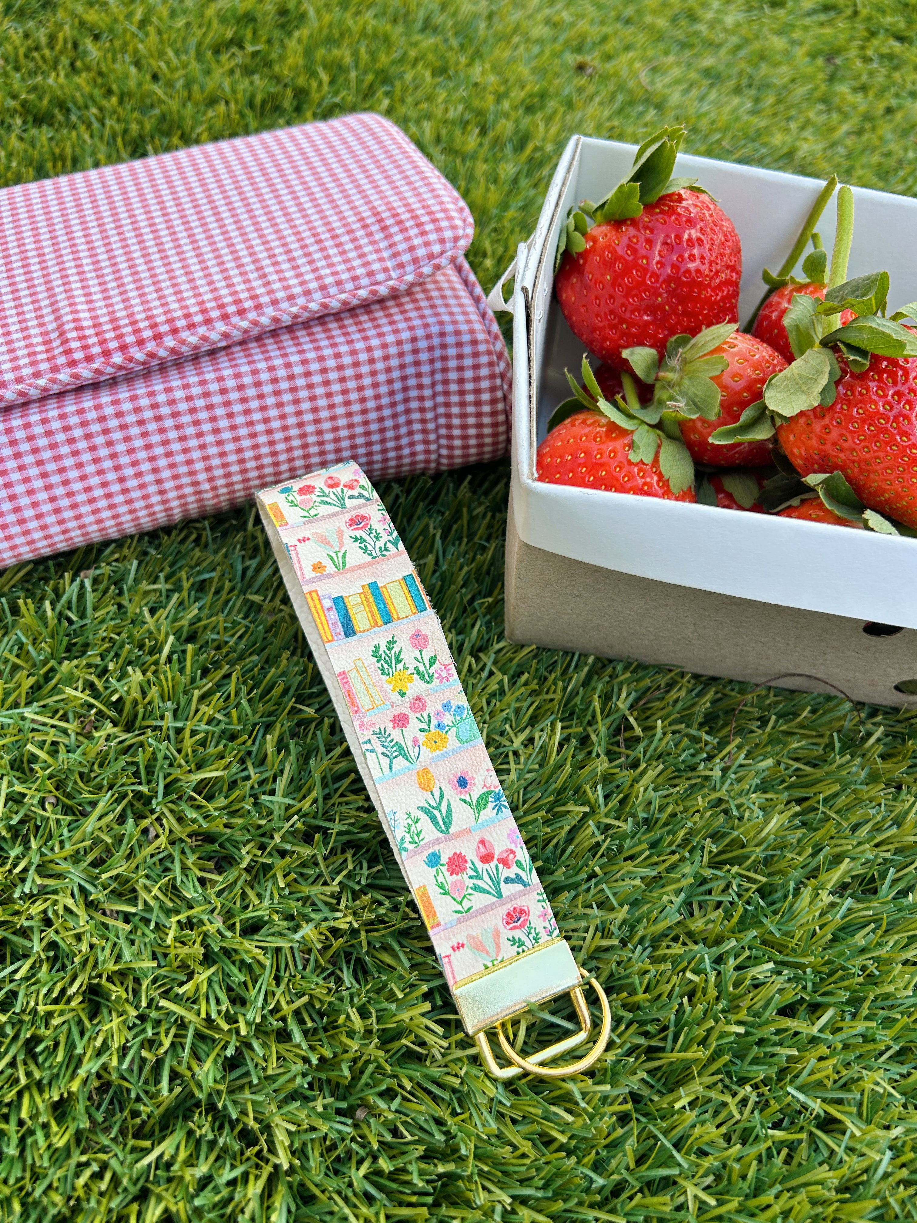 Cream floral bookshelf print wristlet keychain by Sundazed — Book Lover Wristlet flat lay on grass