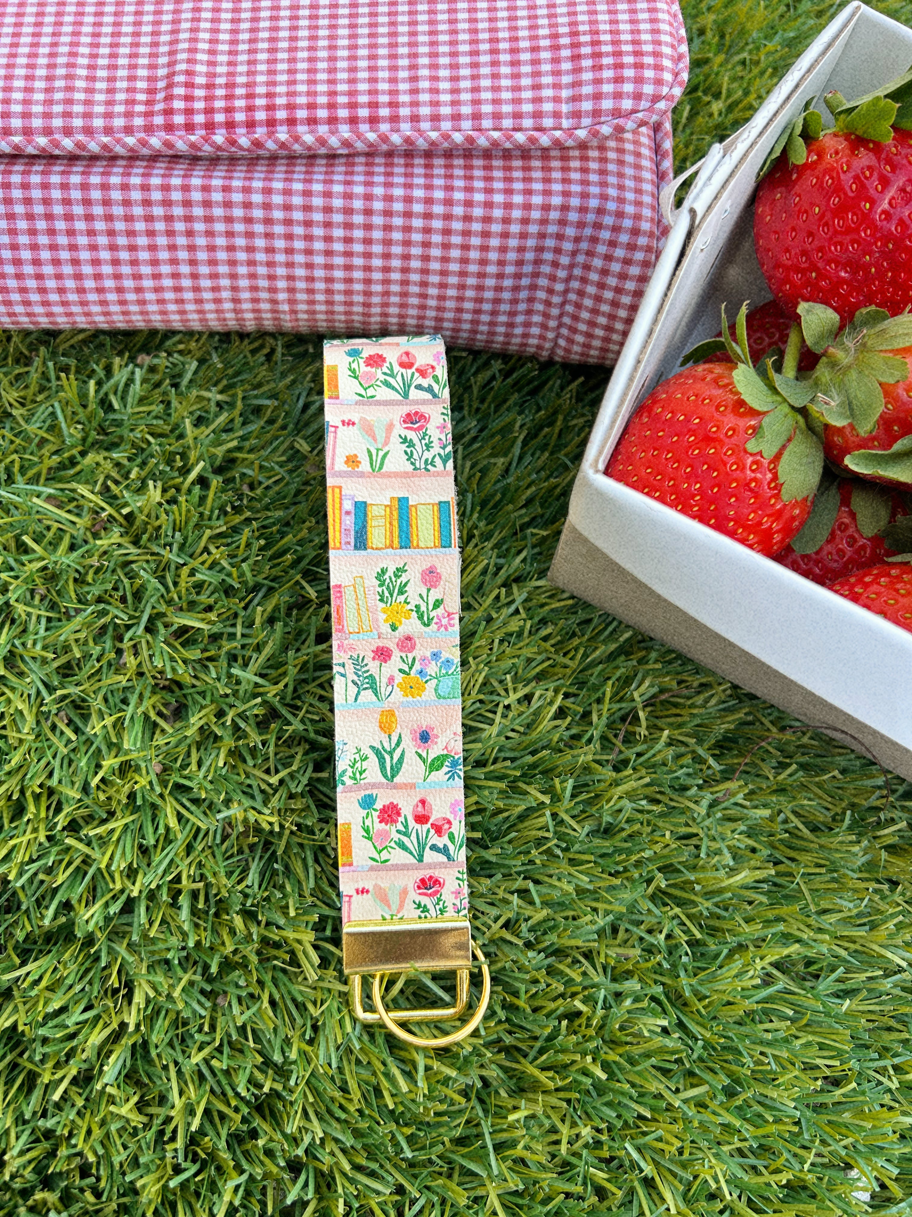 Cream floral bookshelf print wristlet keychain by Sundazed — Book Lover Wristlet flat lay on grass