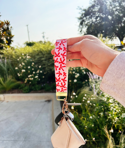 Blush pink bow-print faux leather wristlet keychain for women by Sundazed — flat lay on neutral background Bow & Go wristlet keychain worn on wrist with gold-toned split ring and car keys attached.