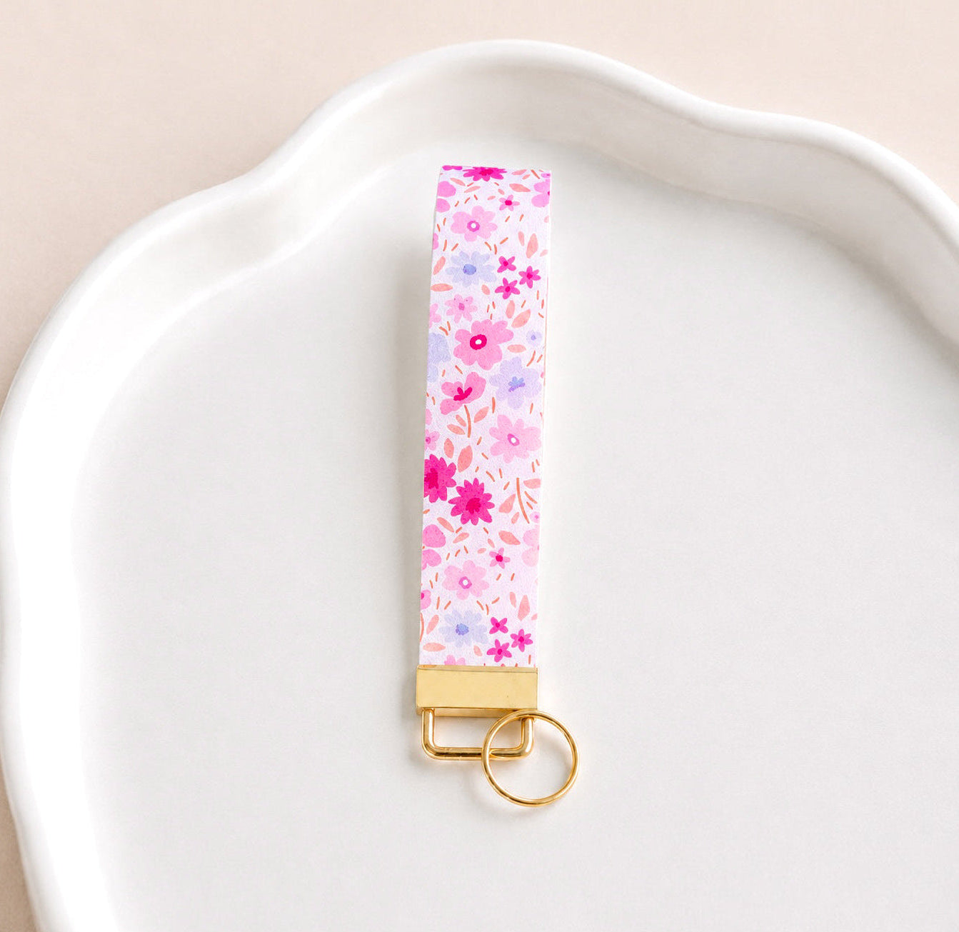 Floral Daydream wristlet keychain with hot pink, blush, lavender, and periwinkle ditsy daisy print on white, laid on white scalloped tray with gold hardware