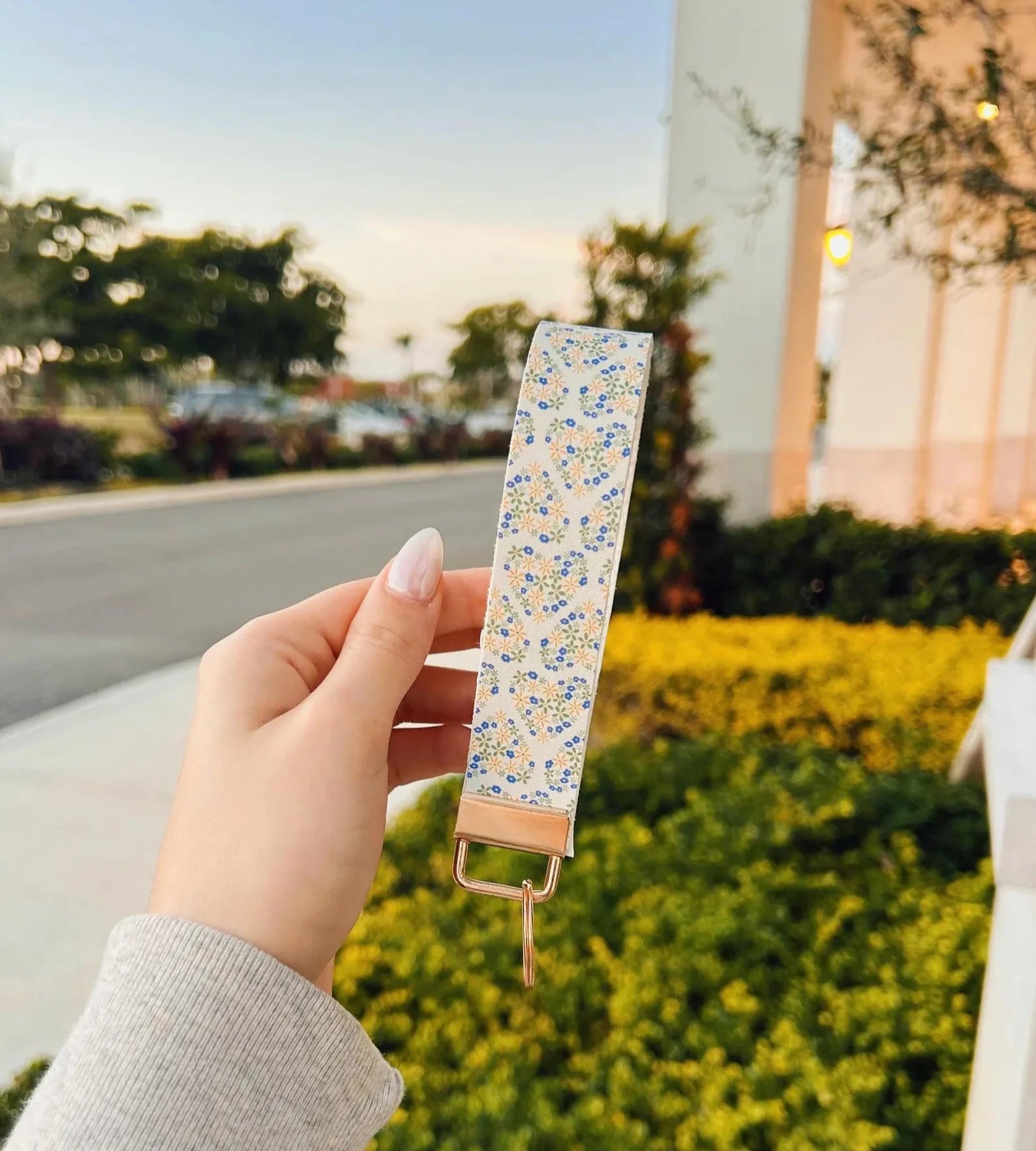 Floral Hearts Wristlet keychain with tiny blue and cream flowers in heart shapes on cream background with gold hardware held outdoors at golden hour
