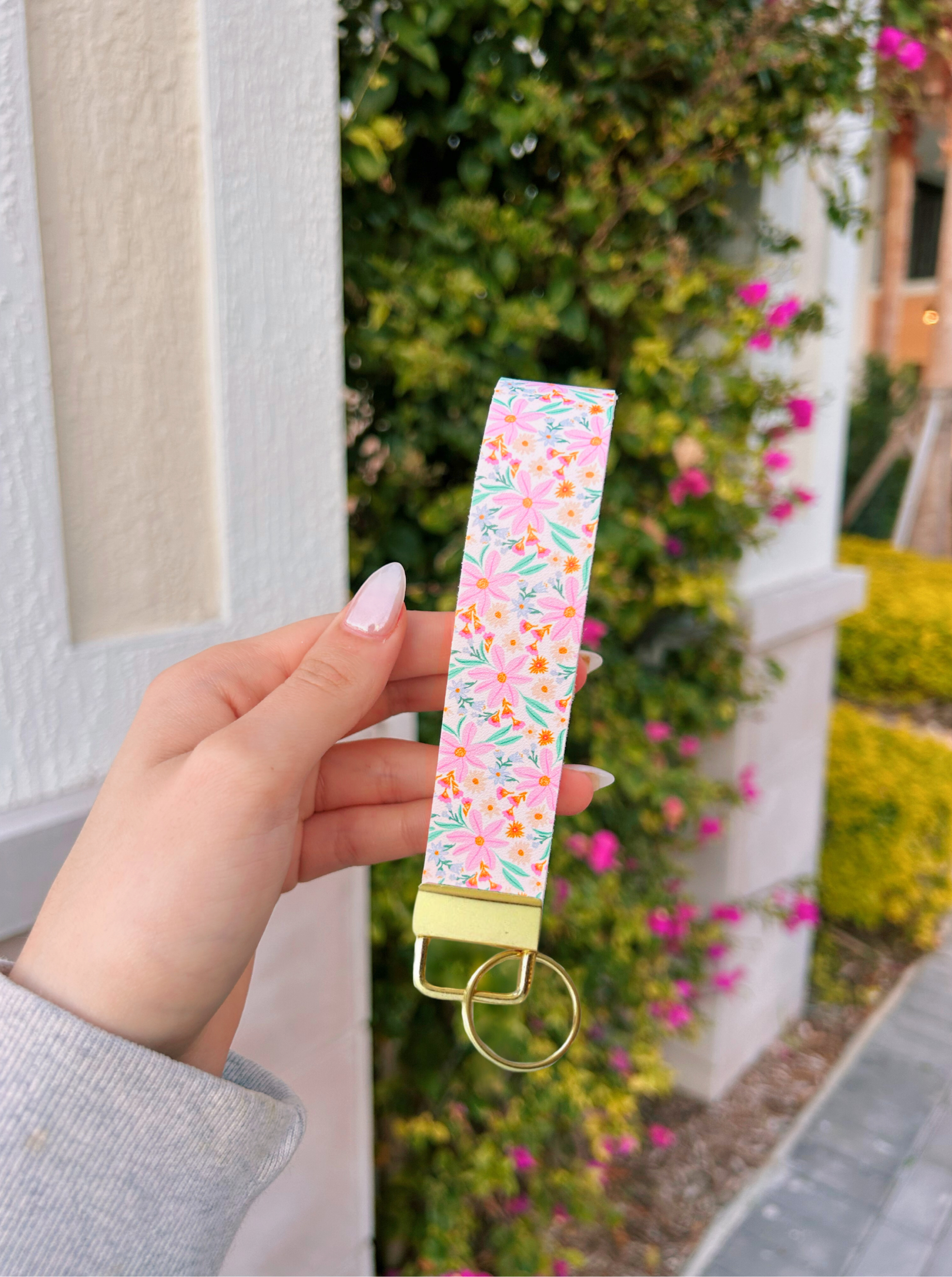 Hand holding a floral keychain with a blurred outdoor background with flowers