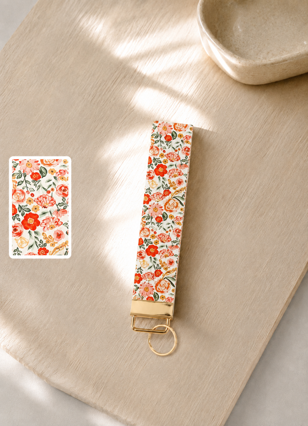 Sweet Meadow floral wristlet keychain with orange, coral, blush, and peach blooms on cream, laid flat on a wood surface with gold hardware