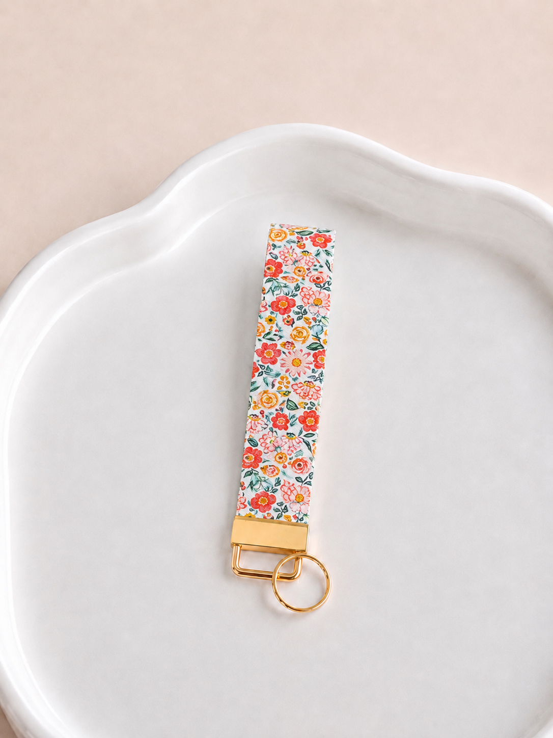 Sweet Meadow wristlet keychain with garden floral print in red, coral, and pink on a white scalloped tray with gold clasp
