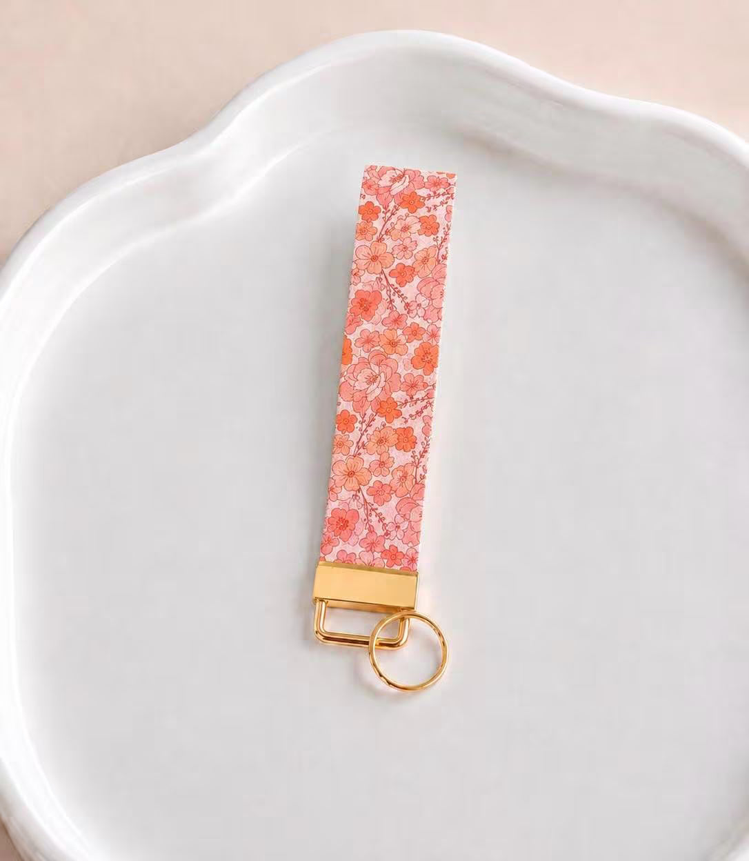 Falling for You wristlet keychain with coral and peach floral print on blush pink base, laid on white scalloped tray with gold hardware
