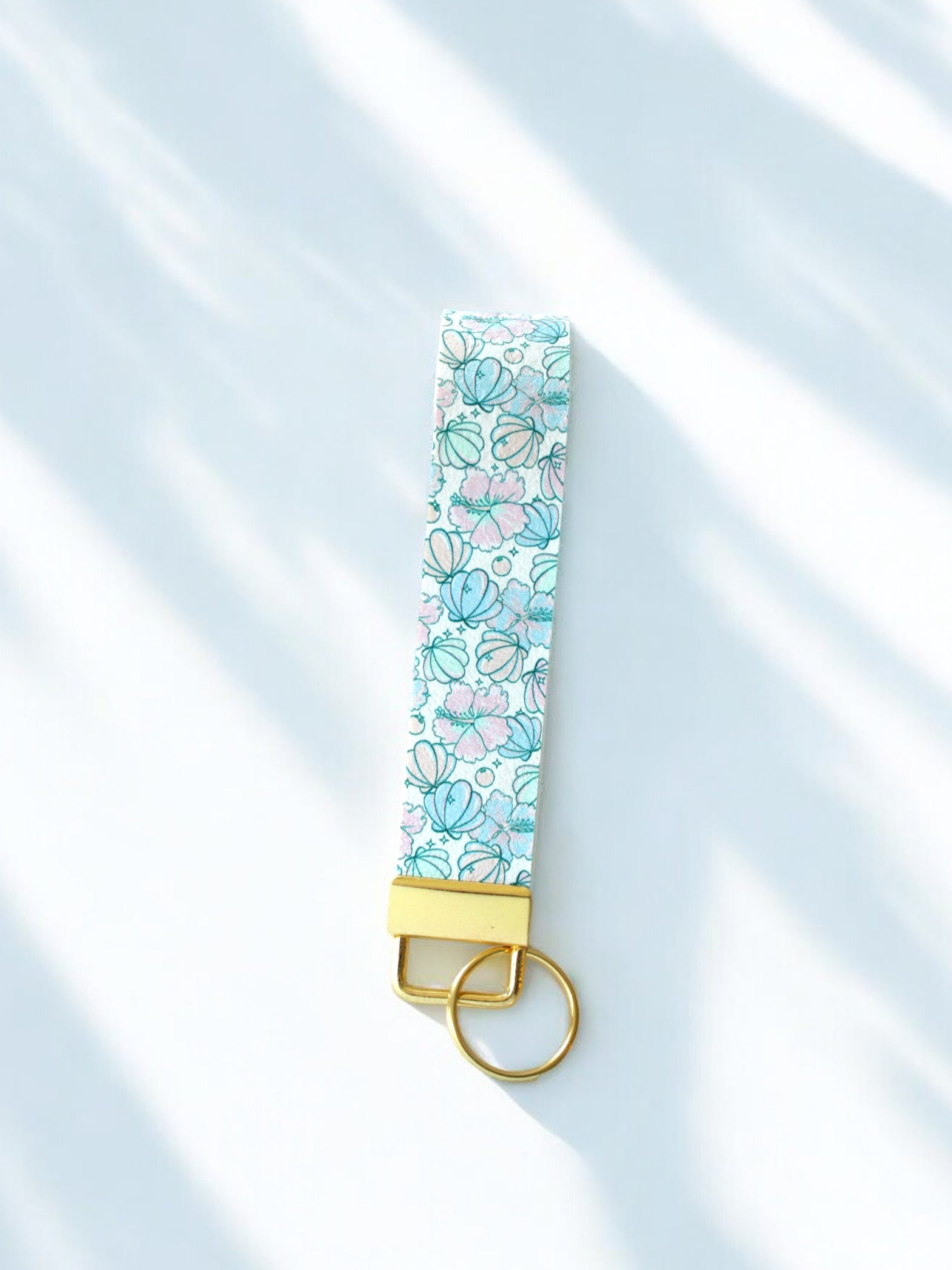 Under the Sea wristlet keychain with delicate seashell print in aqua, mint, and blush pink on white, laid on white white background with gold hardware