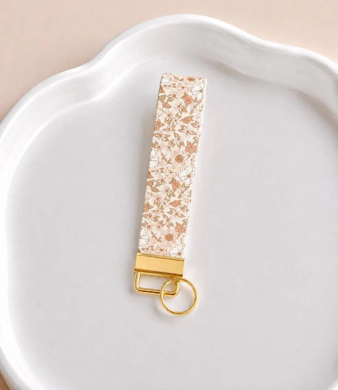 Ella wristlet keychain with delicate ditsy floral print in terracotta, blush, and taupe on cream base, laid on white scalloped tray with gold hardware